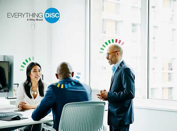 Three business professionals are having a meeting in a modern office. Two are seated, one is standing and speaking. Colored diagrams appear above their heads. The "Everything DiSC" logo is visible in the top left corner.