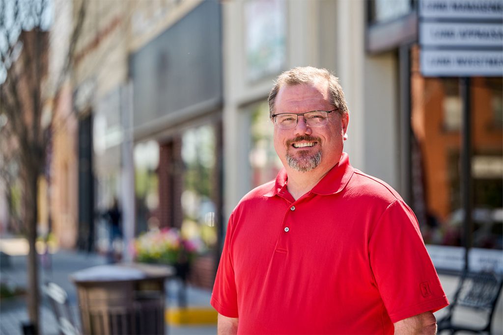 Nick smiling in a red polo in front of a shopping street background. Landscape orientation